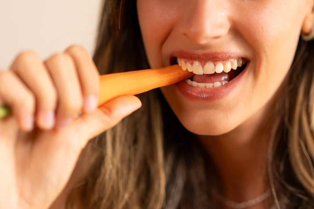 eat-your-way-to-a-brighter-smile-foods-for-optimal-oral-health-woman-eating-carrot-vegetables-nutrition-healthy-diet-folic-acid-periodontal-disease-dark-chocolate-Dental-Finds